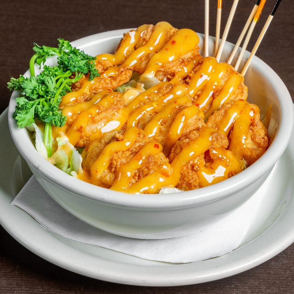 Fried shrimp with orange sauce and parsley in a white bowl, with wooden skewers.
