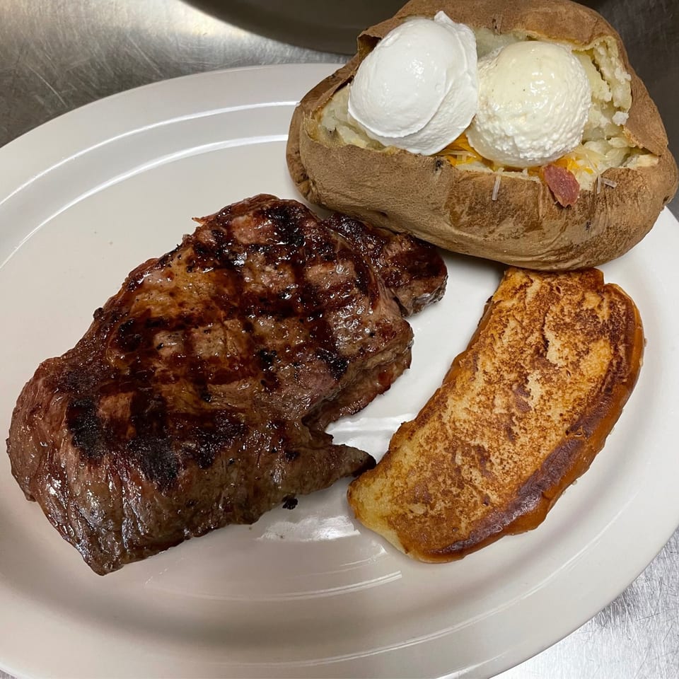 Grilled steak, baked potato with sour cream and butter, and a slice of Texas toast on a white plate.