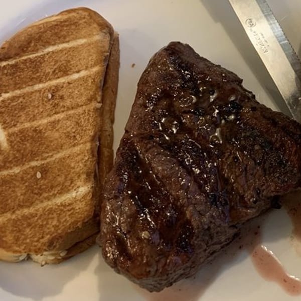 Grilled steak with a side of toasted bread and a knife on a white plate.