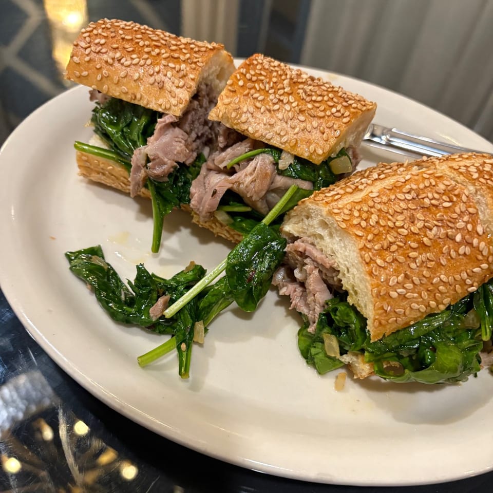 Two halves of a steak and spinach sandwich on a sesame seed baguette, served on a white plate.