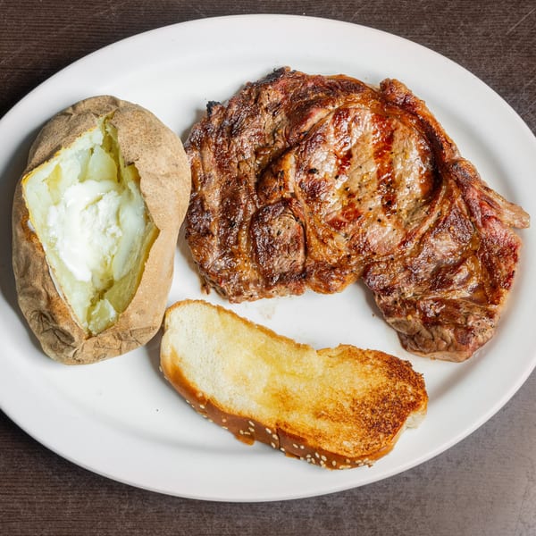 Grilled steak, a baked potato with sour cream, and toasted bread on a white plate.